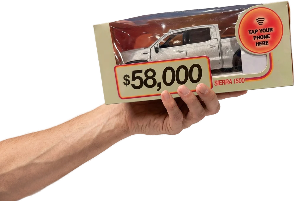 A hand holding the Motibox - a serialized box with a die-cast 2026 Sierra 1500 and a tap-to-book NFC sticker